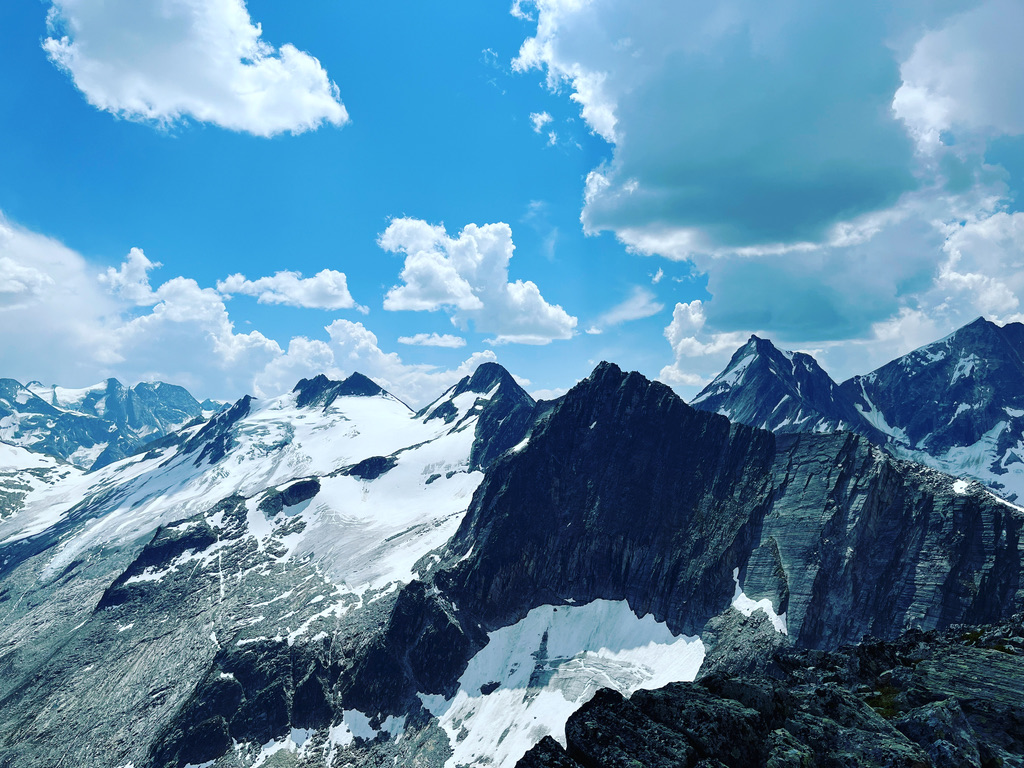 Rugged alpine peaks and snowfields beneath a blue sky and clouds